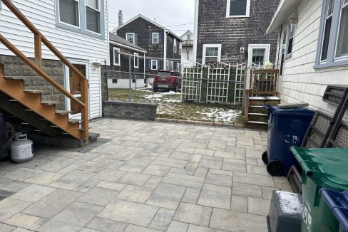 A backyard with a brick patio and a trash can.