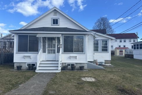 A small white suburban house with a screened front porch and a tidy lawn.