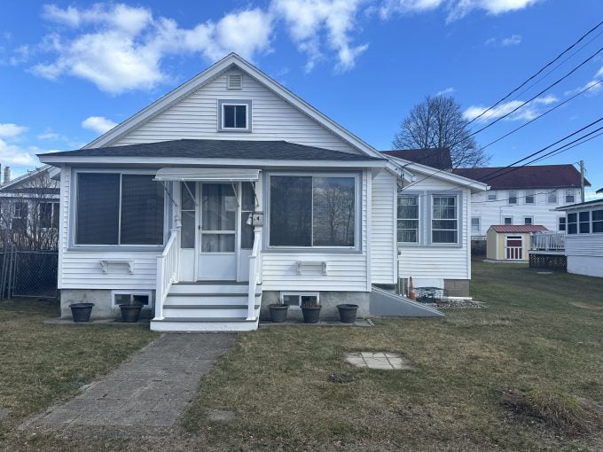 A small white suburban house with a screened front porch and a tidy lawn.