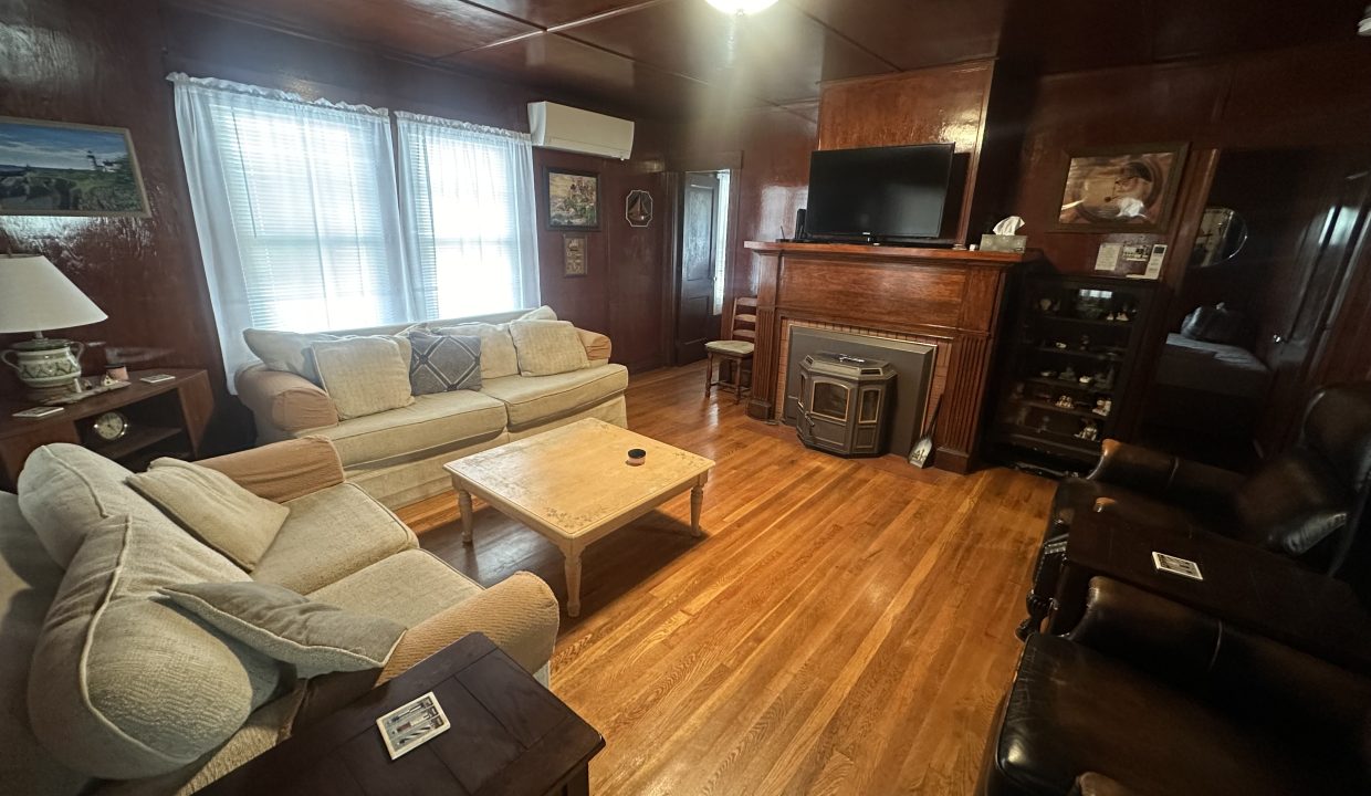 A cozy living room with wooden paneling, hardwood floor, a beige sofa, a television, and vintage furnishings.