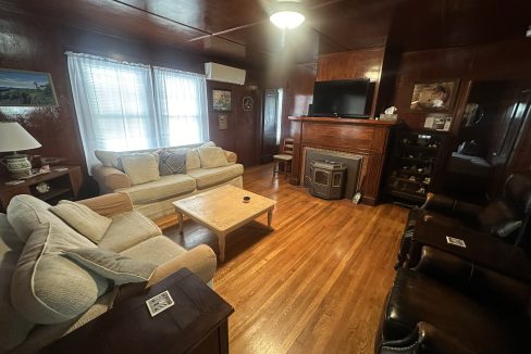 A cozy living room with wooden paneling, hardwood floor, a beige sofa, a television, and vintage furnishings.