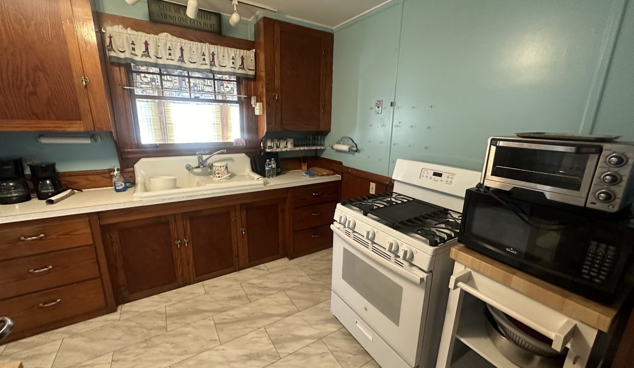 A kitchen with wooden cabinets, blue walls, and various appliances including a microwave, stove, and toaster oven.