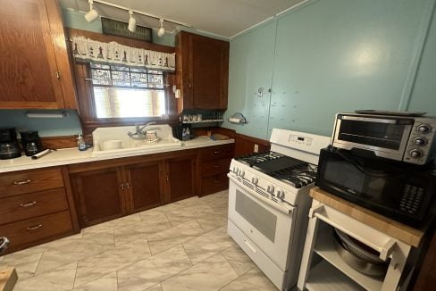 A kitchen with wooden cabinets, blue walls, and various appliances including a microwave, stove, and toaster oven.