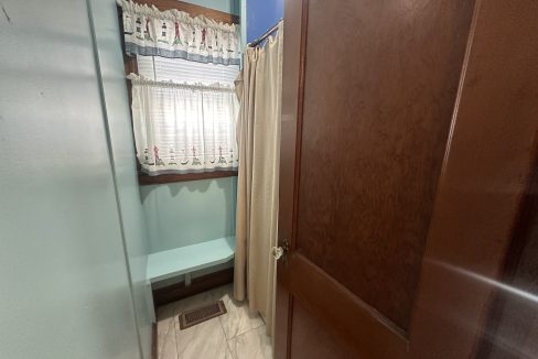 A partially open wooden door revealing a small bathroom with a shower curtain and a window with a valance.