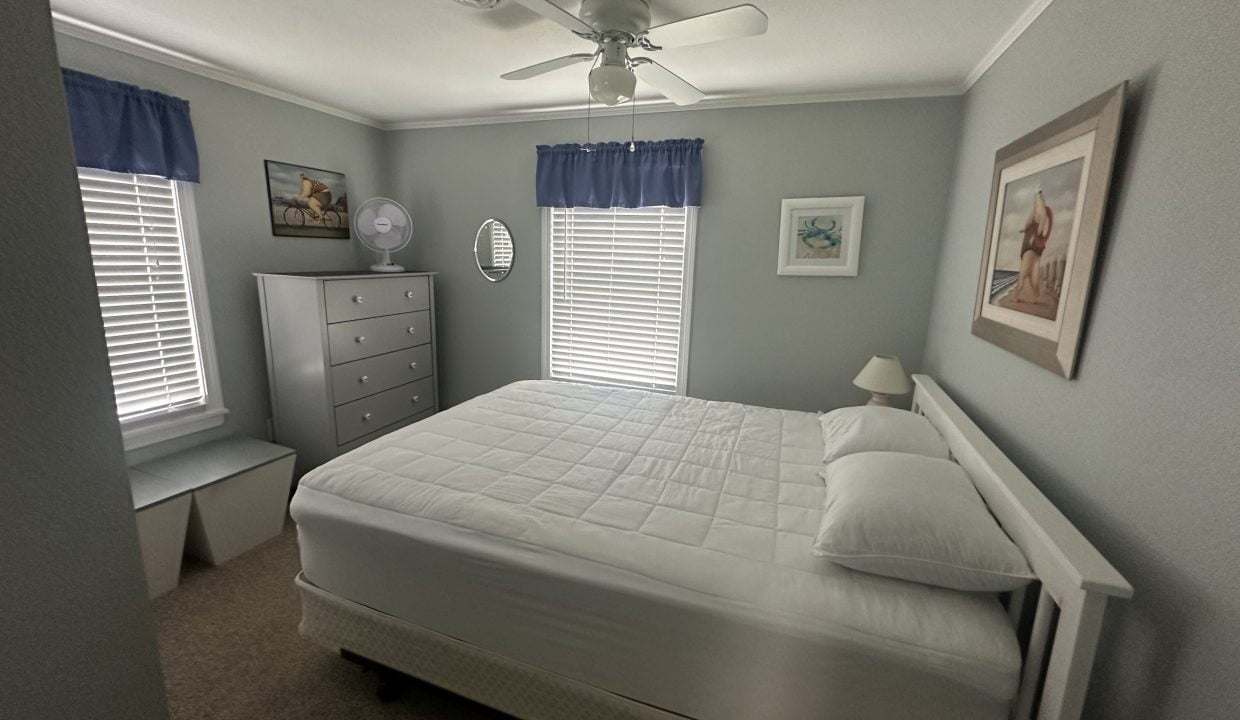 A neatly arranged bedroom with a white bed, grey dresser, and blue accents under soft lighting.