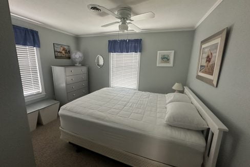 A neatly arranged bedroom with a white bed, grey dresser, and blue accents under soft lighting.