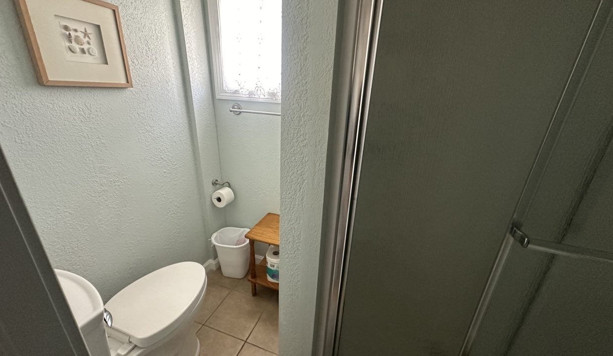 Small bathroom with a toilet, corner shower, and a window with blinds.