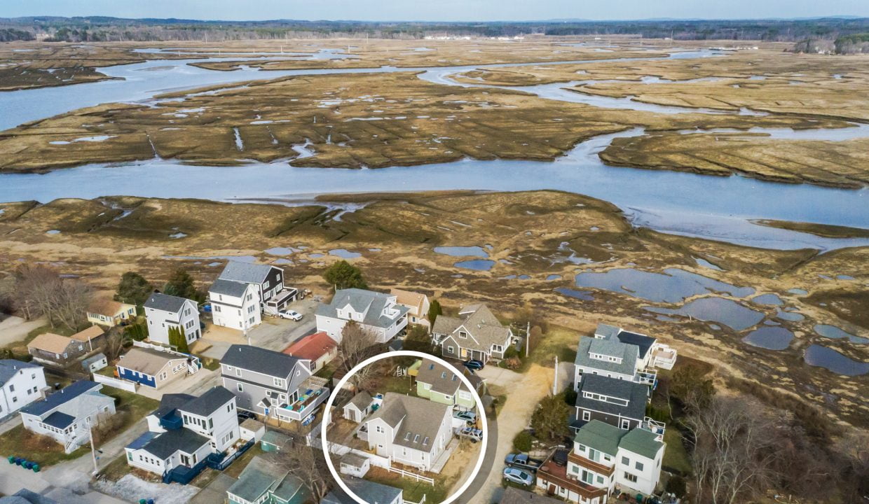 Aerial view of a coastal residential area with houses adjacent to a meandering tidal marsh.