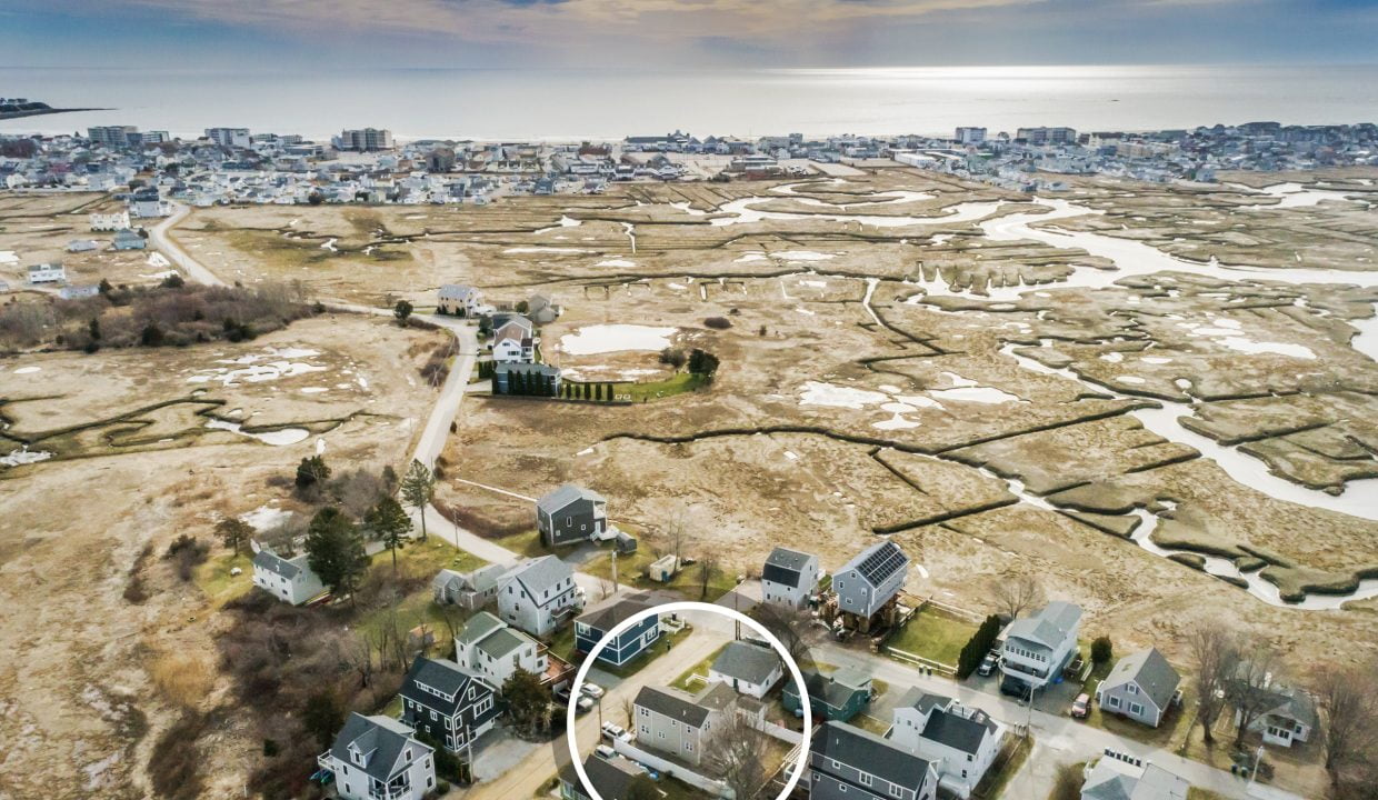 Aerial view of a coastal neighborhood near wetlands with outlined property indicating focus on a specific house.