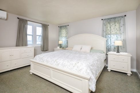 A bedroom with a white bed and dresser.