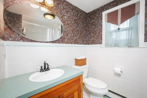 A bathroom with a toilet, sink and a mirror.