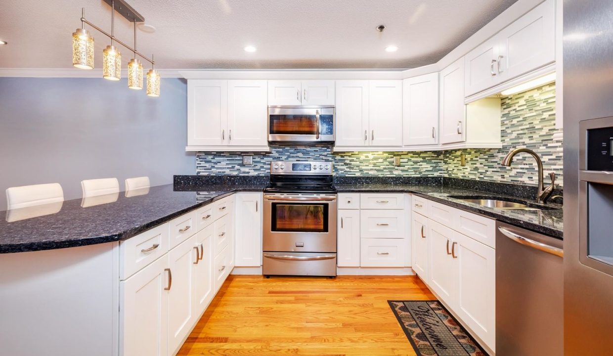 A kitchen with white cabinets and black counter tops.