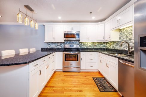 A kitchen with white cabinets and black counter tops.