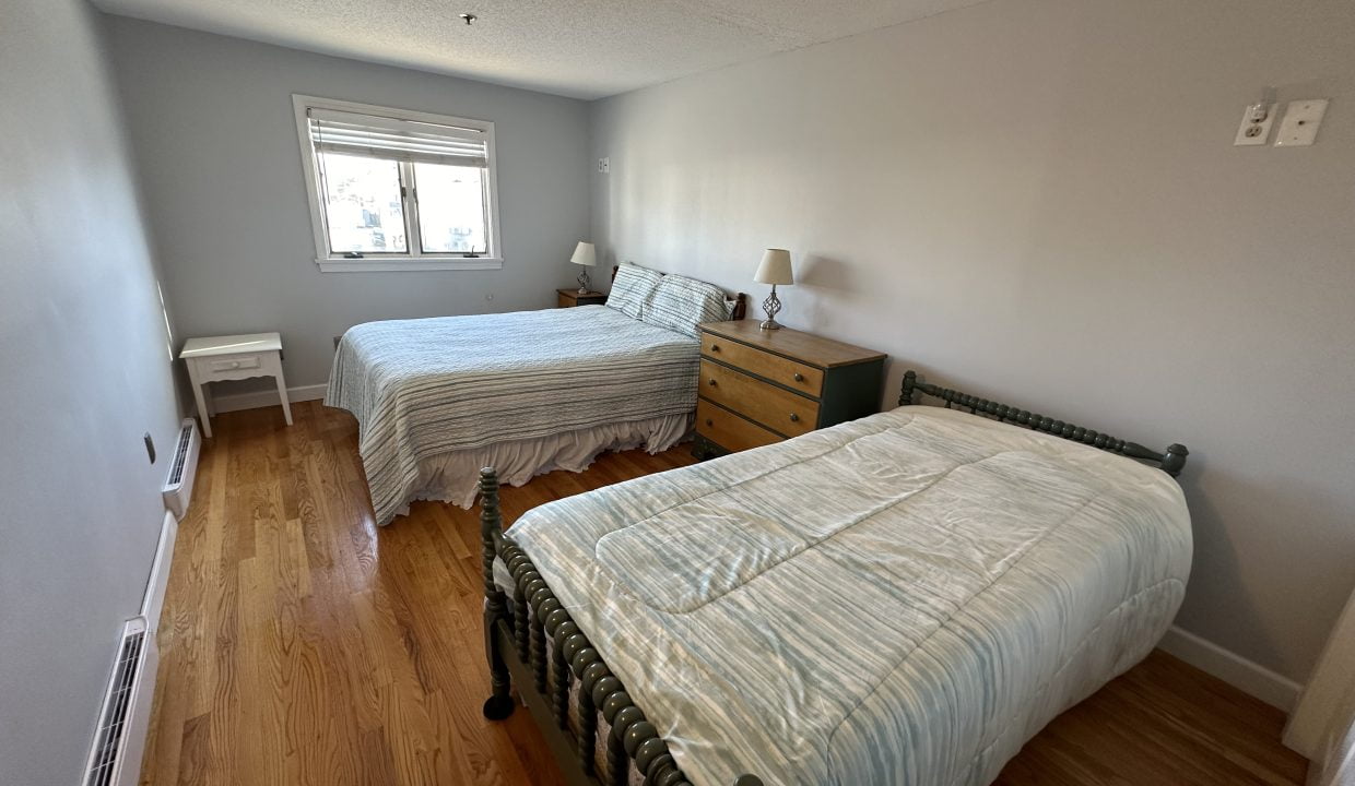 Two beds in a room with hardwood floors.