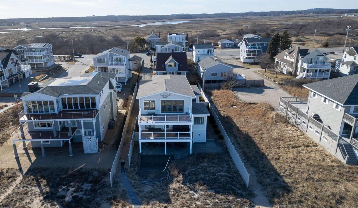 Aerial view of coastal homes with balconies overlooking a beach area with sparse vegetation.