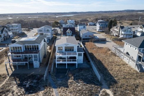 Aerial view of coastal homes with balconies overlooking a beach area with sparse vegetation.