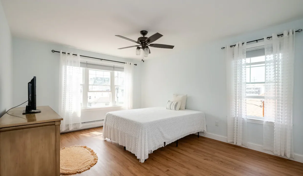 Bright, minimalistic bedroom with a single bed, ceiling fan, and hardwood floors.