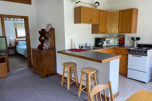 Compact kitchen with wooden cabinets and breakfast bar, adjacent to a small living area with a vintage television.