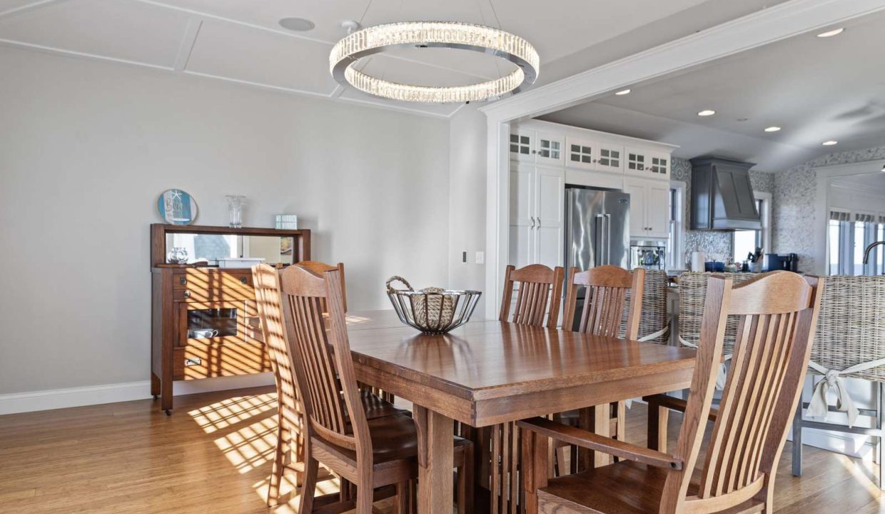 A spacious dining room featuring a large wooden table with chairs and an elegant chandelier.
