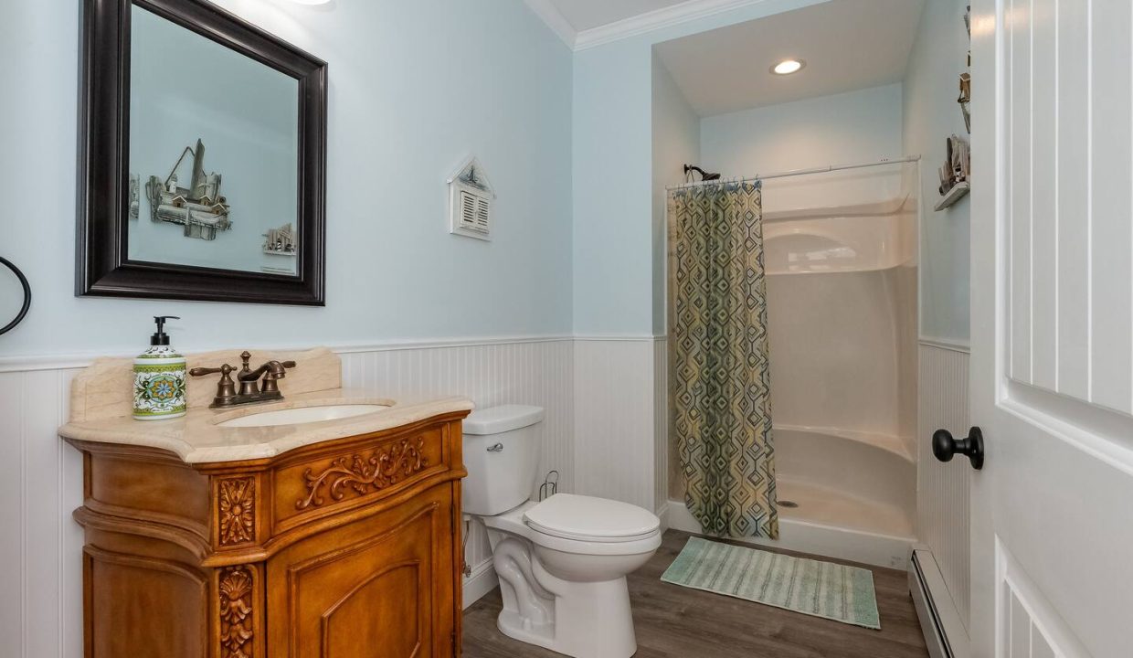 A clean and neatly organized bathroom with a wooden vanity, white toilet, and a shower with a patterned curtain.