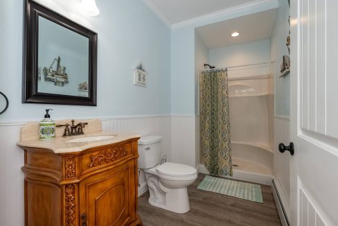 A clean and neatly organized bathroom with a wooden vanity, white toilet, and a shower with a patterned curtain.