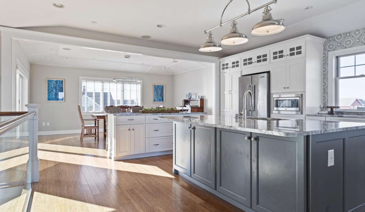 Modern kitchen interior with white cabinets, stainless steel appliances, and a central island under natural lighting.