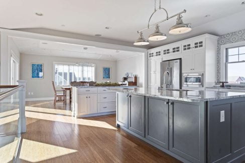 Modern kitchen interior with white cabinets, stainless steel appliances, and a central island under natural lighting.