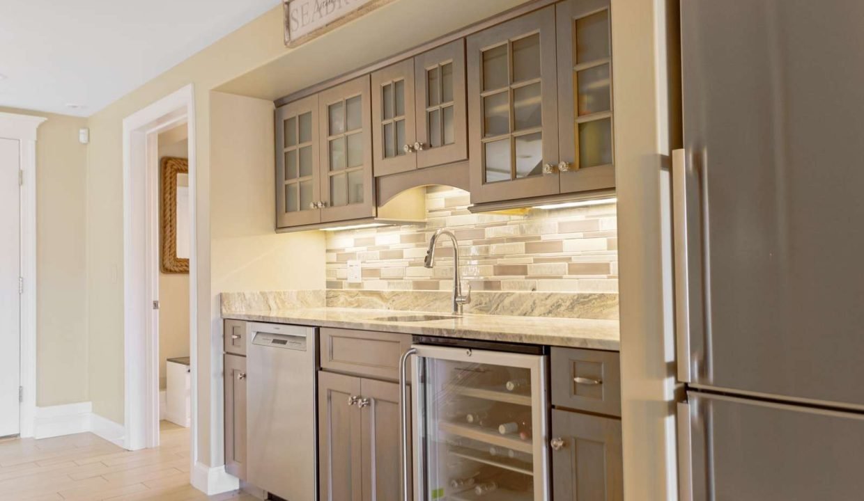 A modern kitchen corner featuring stainless steel appliances, beige tile backsplash, granite countertop, and wooden cabinetry.