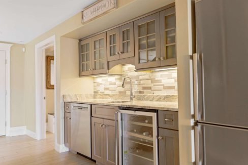 A modern kitchen corner featuring stainless steel appliances, beige tile backsplash, granite countertop, and wooden cabinetry.