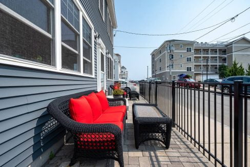 Outdoor patio furniture positioned alongside a residential building on a narrow paved space.