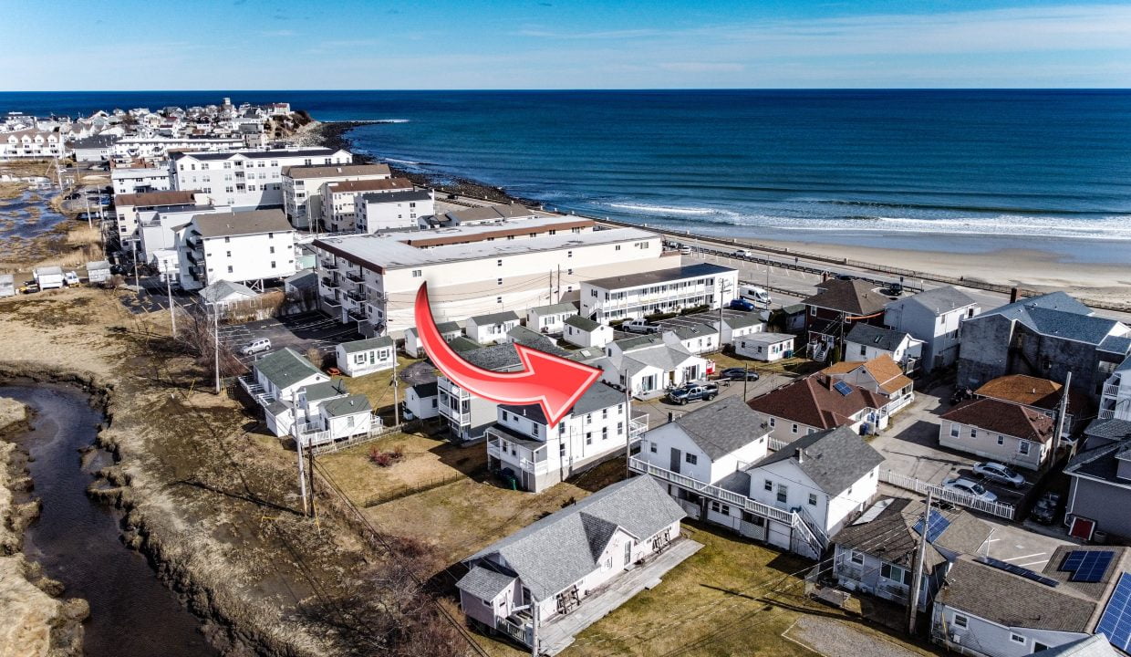 Aerial view of a coastal residential area with an arrow pointing to a specific building near the beach.