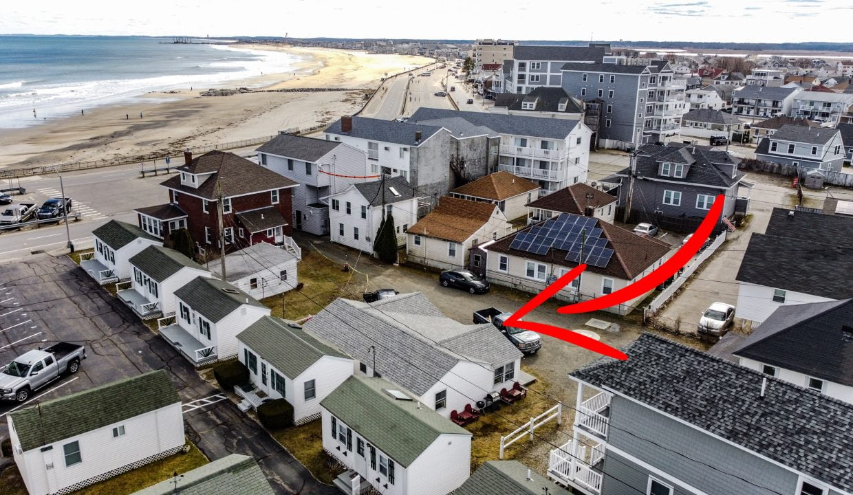 Aerial view of a coastal neighborhood with an arrow highlighting a specific house near a beach.