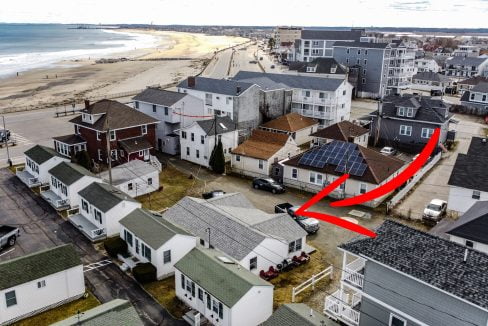 Aerial view of a coastal neighborhood with an arrow highlighting a specific house near a beach.