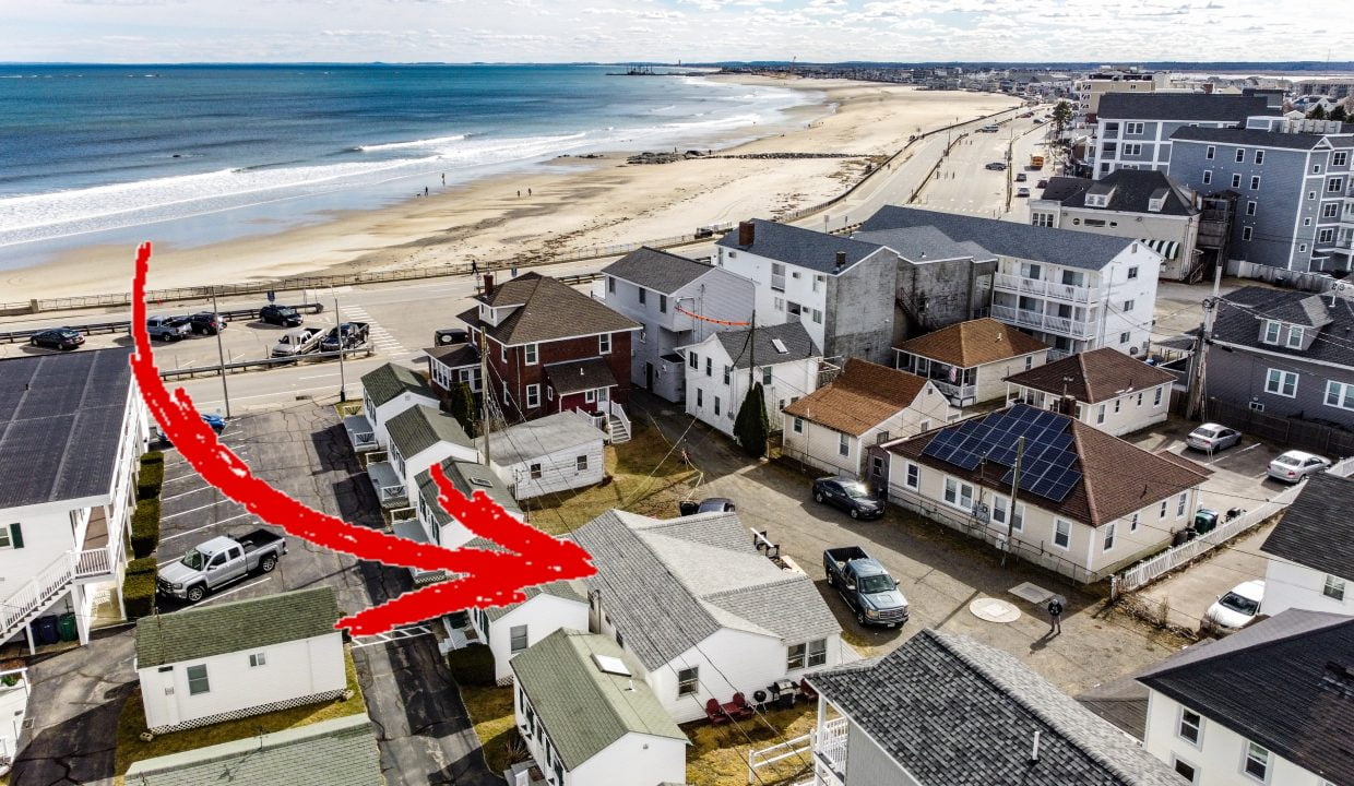 Aerial view of a coastal residential neighborhood with a red arrow drawn over the image pointing to the beach.