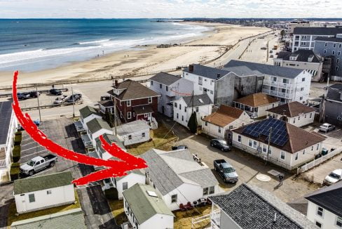 Aerial view of a coastal residential neighborhood with a red arrow drawn over the image pointing to the beach.