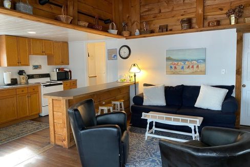 A cozy, wood-paneled living space with an open kitchen, couch, coffee table, and reclining chairs.