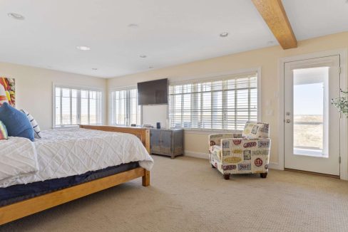Spacious, well-lit bedroom with a large bed, multiple windows, and a door leading outside.