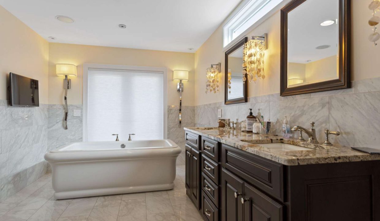 A bright, modern bathroom with marble walls, a freestanding bathtub, double vanity sinks, and an elegant chandelier.