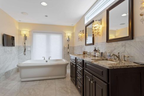 A bright, modern bathroom with marble walls, a freestanding bathtub, double vanity sinks, and an elegant chandelier.