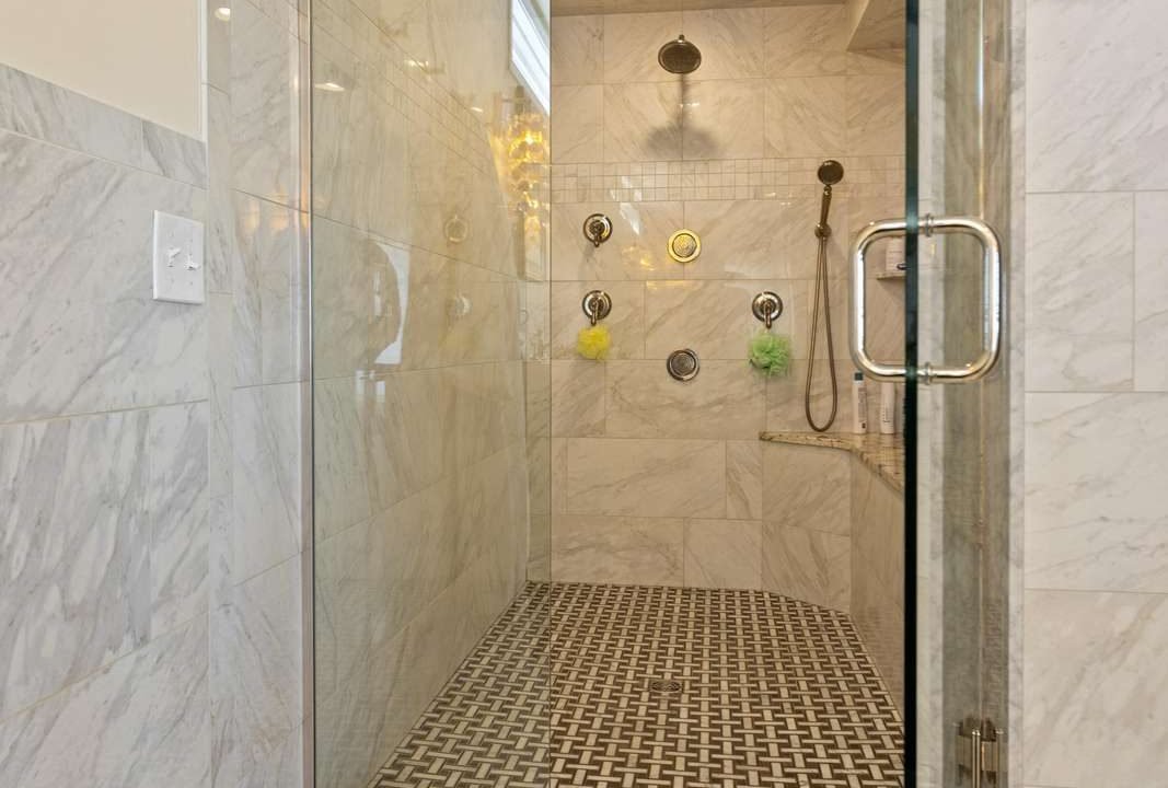 Modern bathroom with marble tiles featuring a glass-door shower with multiple shower heads.