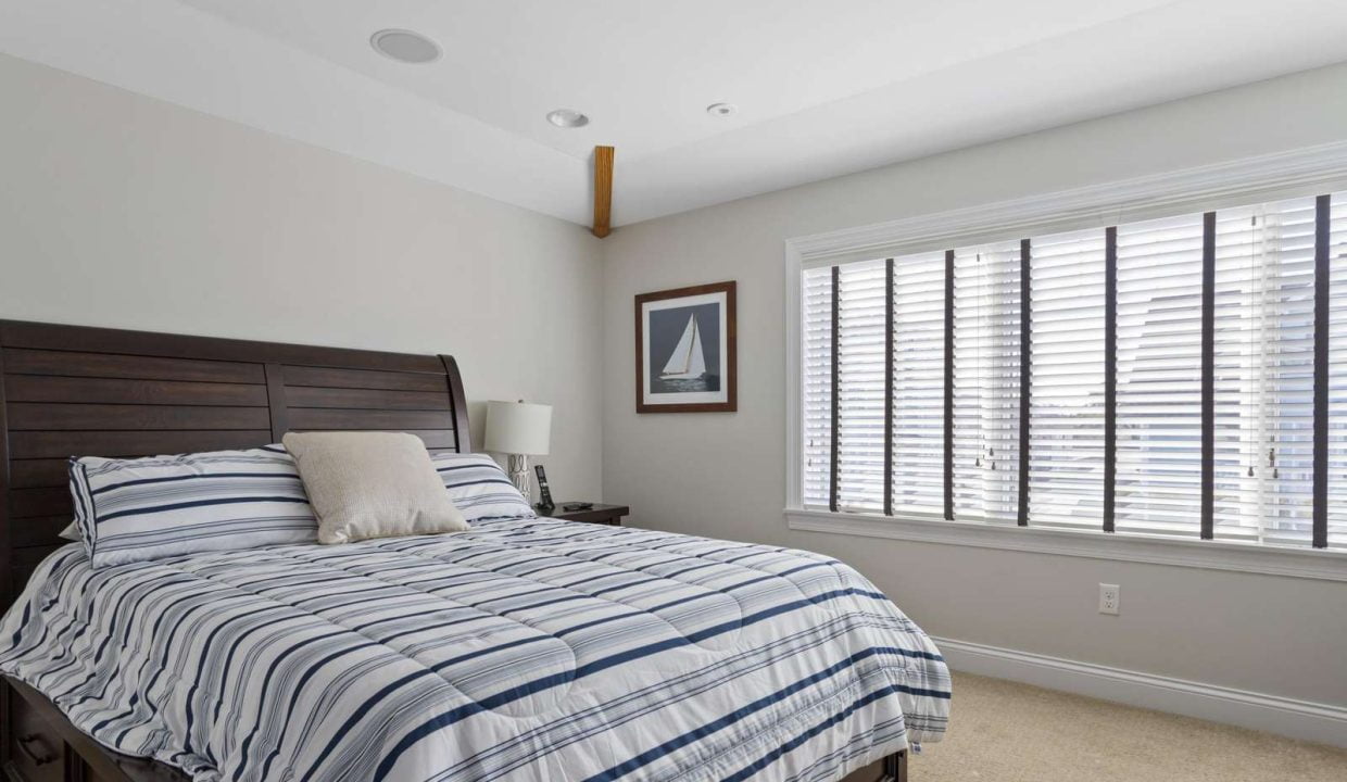 A neatly arranged bedroom with a striped bedcover, wooden headboard, and a window with closed blinds.