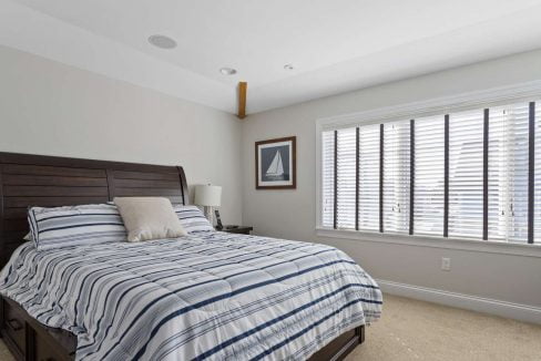 A neatly arranged bedroom with a striped bedcover, wooden headboard, and a window with closed blinds.