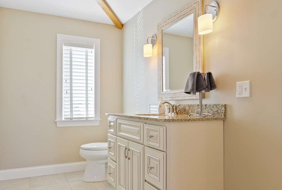 A clean and well-lit bathroom with a vanity cabinet, mirror, and toilet.