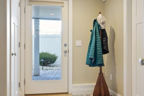 A clean and tidy hallway with wooden floors, a coat rack by the door, and a striped rug.