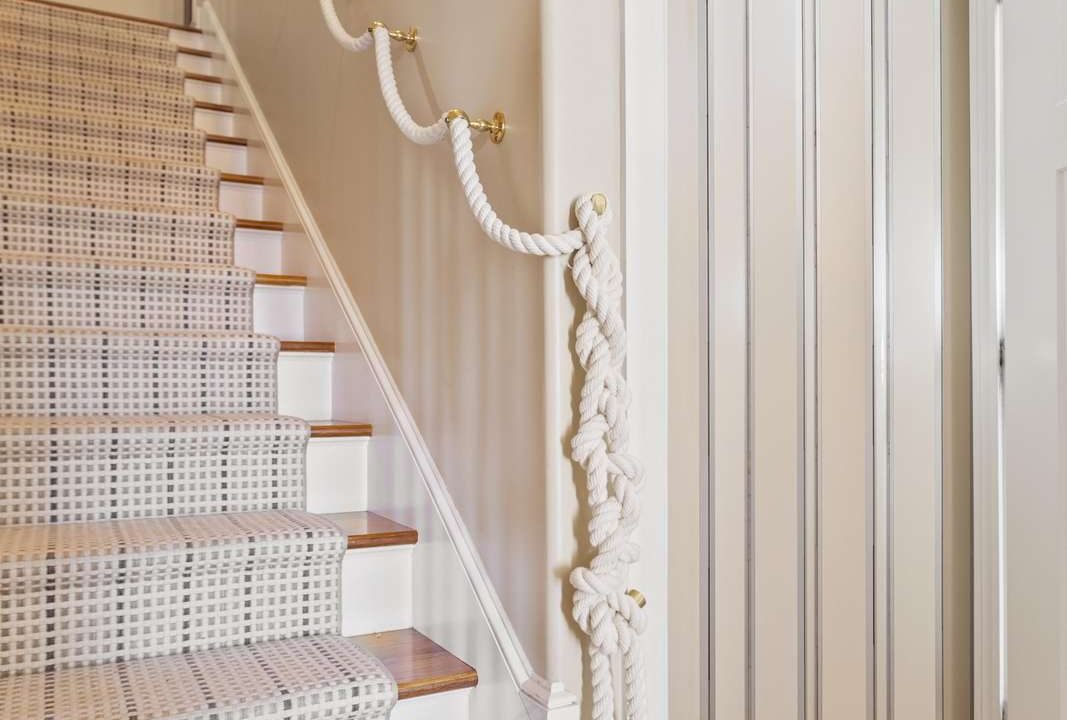 Elegant staircase with white carpet and nautical-themed rope banister.