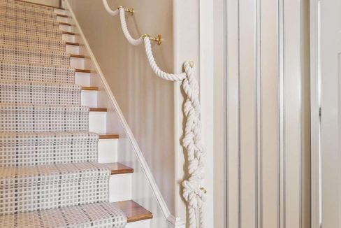 Elegant staircase with white carpet and nautical-themed rope banister.