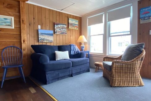 Cozy living room with a blue sofa, wooden and wicker chairs, and seaside-themed decor.