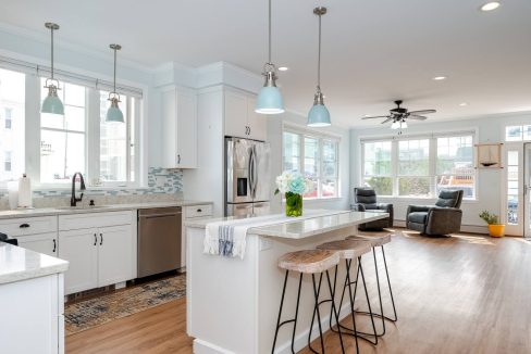 A modern kitchen with white cabinetry, stainless steel appliances, and a central island with bar stools under pendant lights.