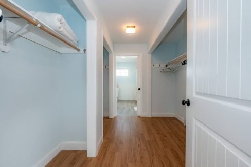 A clean and empty hallway in a modern house with wooden flooring, white walls, and built-in closets.
