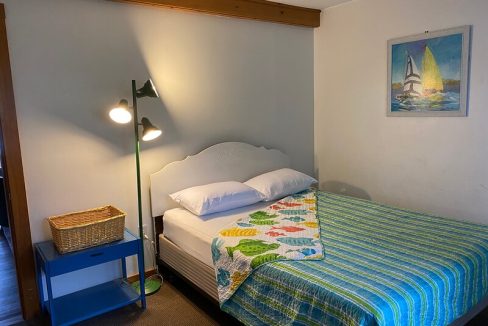 A cozy bedroom with a made bed, a floor lamp, and nautical-themed decor.